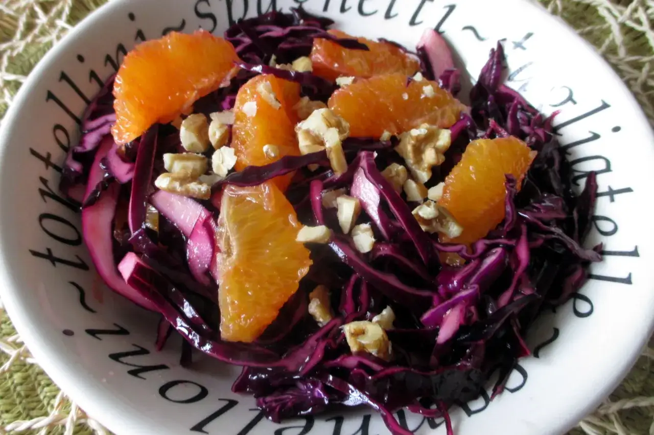 Insalata di cavolo rosso con spicchi d'arancia e noci tritate, un piatto colorato e croccante.