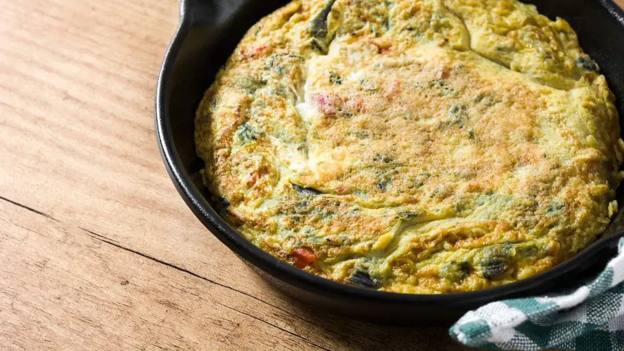 Frittata dorata con fiori di zucca, cotta in padella, su un tavolo di legno.