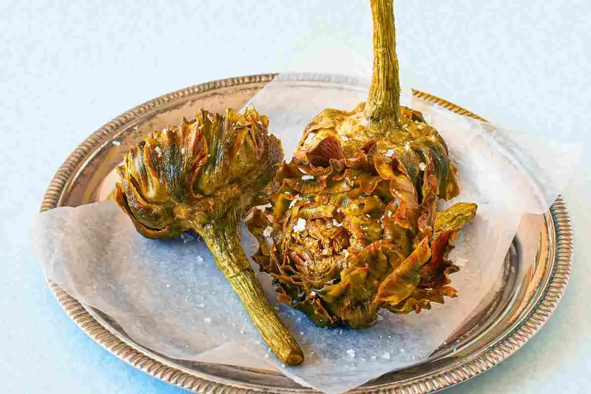 Due carciofi alla giudia dorati e croccanti, cosparsi di sale grosso, su un piatto d'argento.