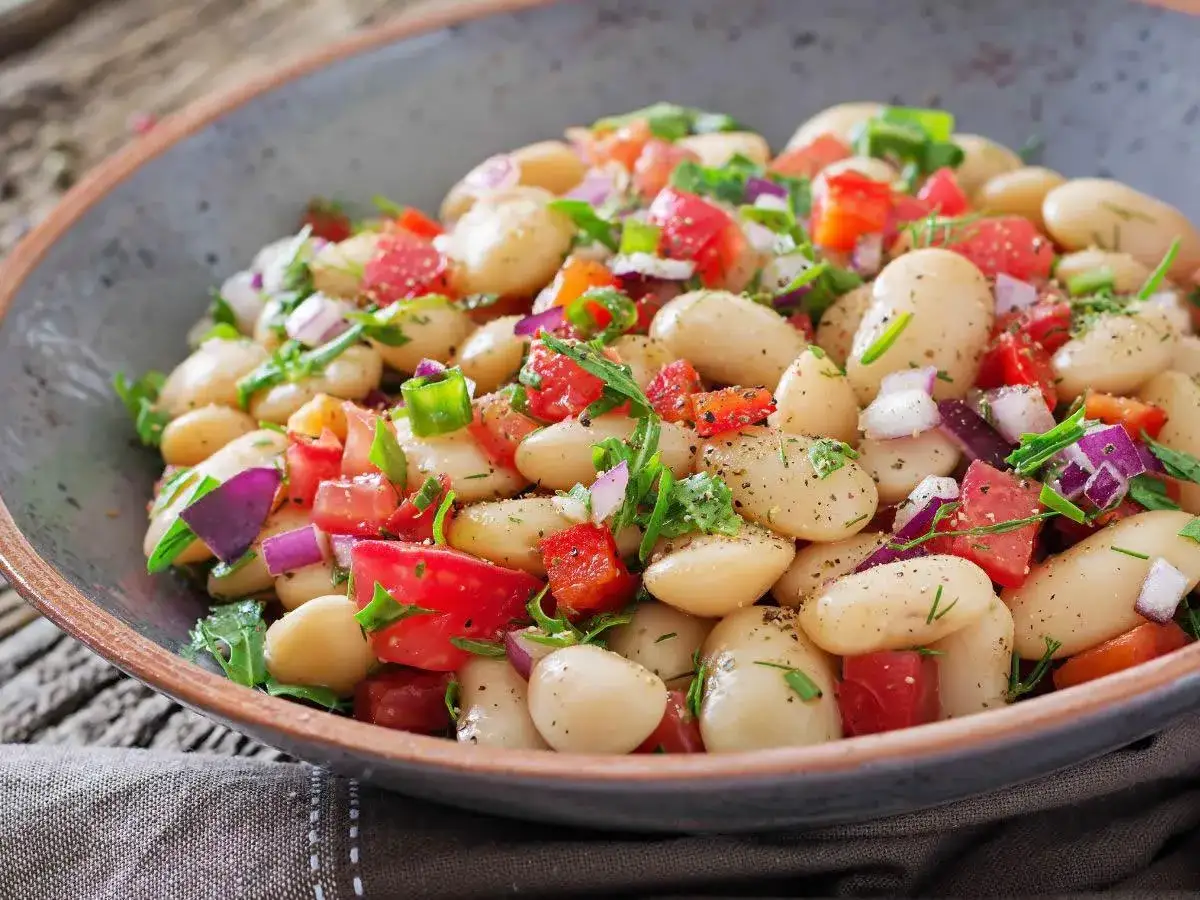 Insalata di fagioli bianchi, pomodori, cipolla rossa e erbe fresche, condita con pepe nero. Un piatto estivo leggero e gustoso.