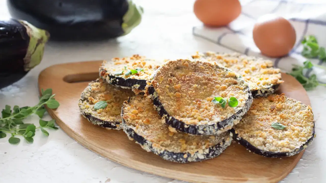 Fette di cordon bleu di melanzane impanate e dorate, servite su un tagliere di legno con erbe aromatiche fresche.