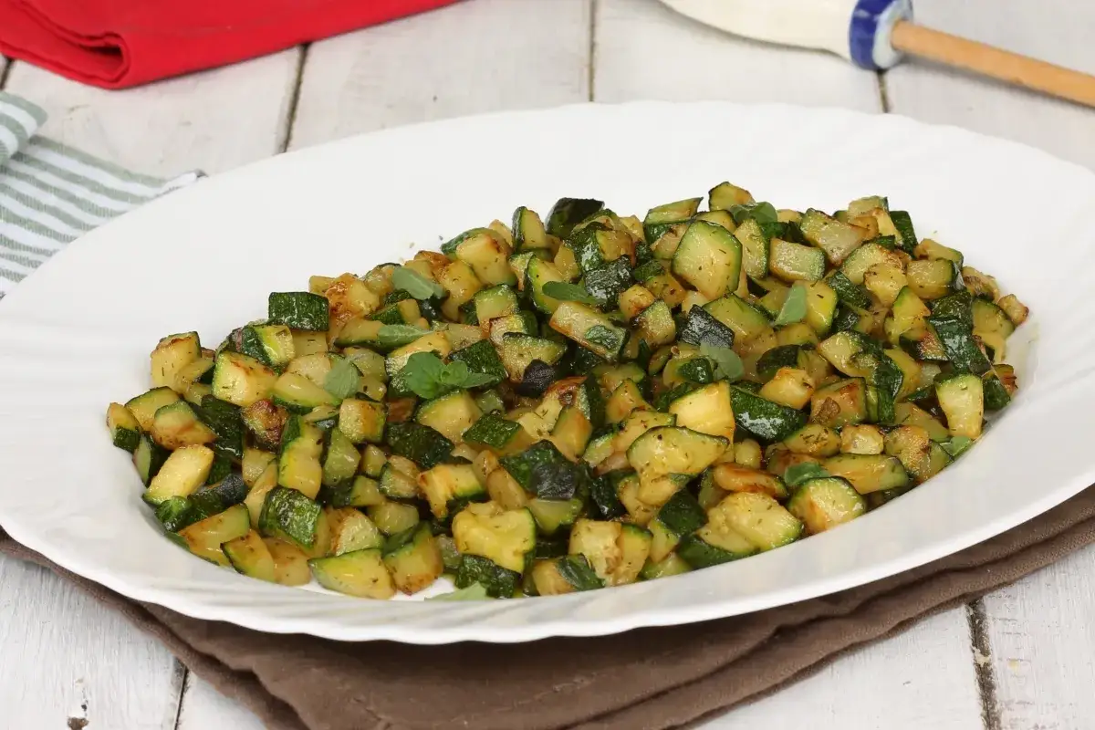 Zucchine in padella sfiziose, tagliate a cubetti e condite con erbe aromatiche, servite su un piatto bianco.