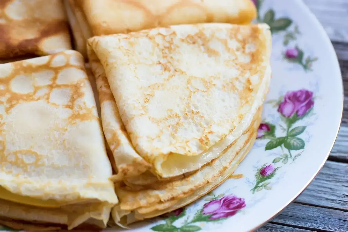 Delicate crepes senza uova, piegate e impilate su un piatto fiorito. Perfette per una colazione leggera o uno spuntino.