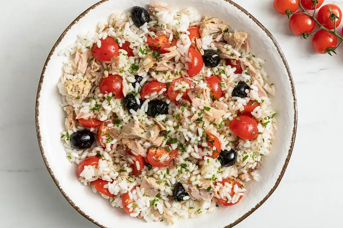 Insalata di riso con tonno, pomodorini, olive nere e prezzemolo. Ingredienti freschi e colorati per un piatto estivo.