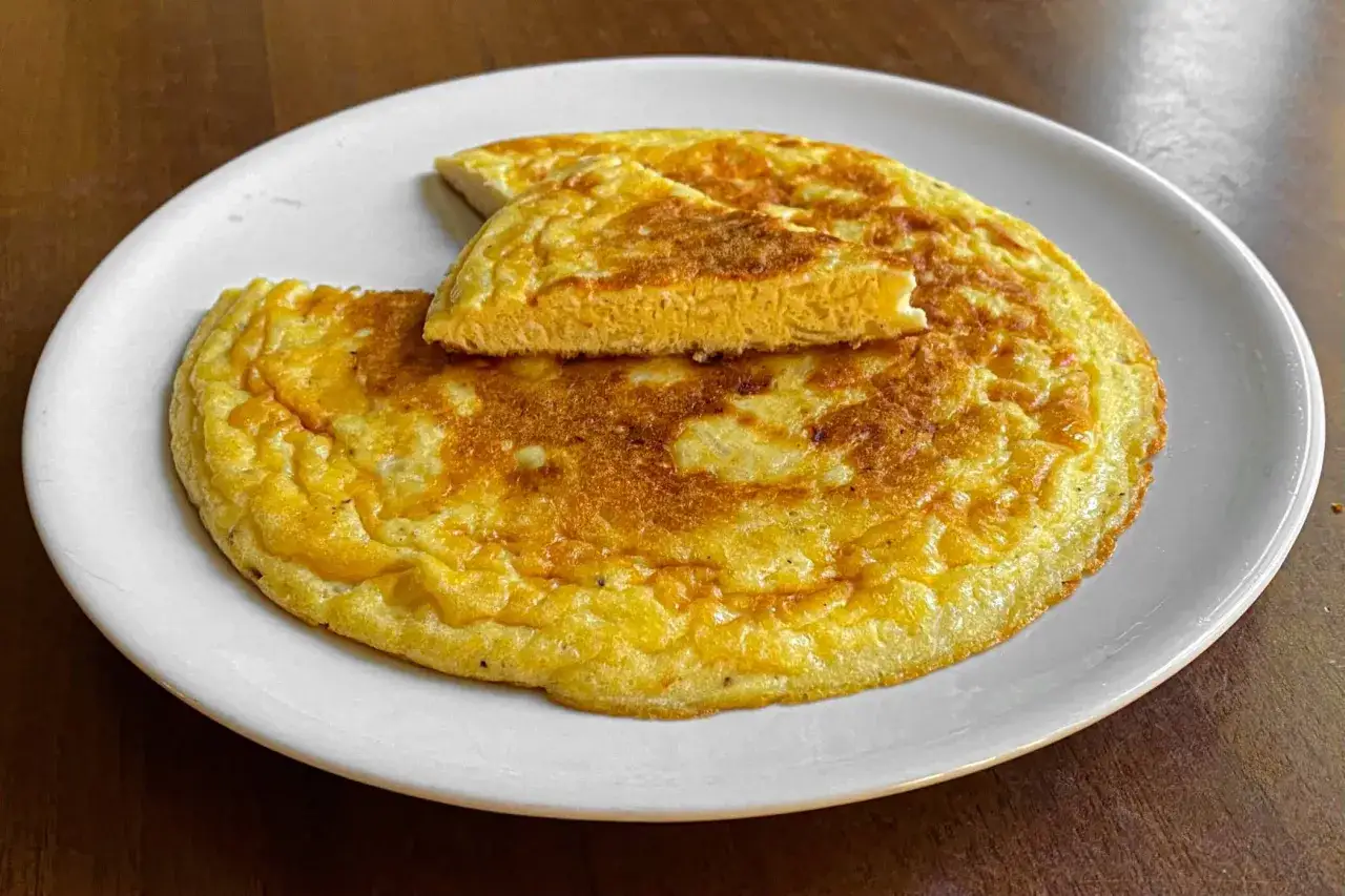 Frittata di cipolle dorata e soffice, servita su un piatto bianco. Una fetta è stata sollevata, mostrando la consistenza interna.