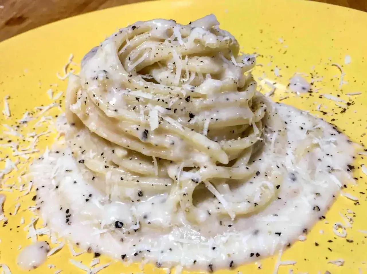 Un piatto di spaghetti cremosi, conditi con abbondante pecorino romano e pepe nero macinato fresco, un classico cacio e pepe.