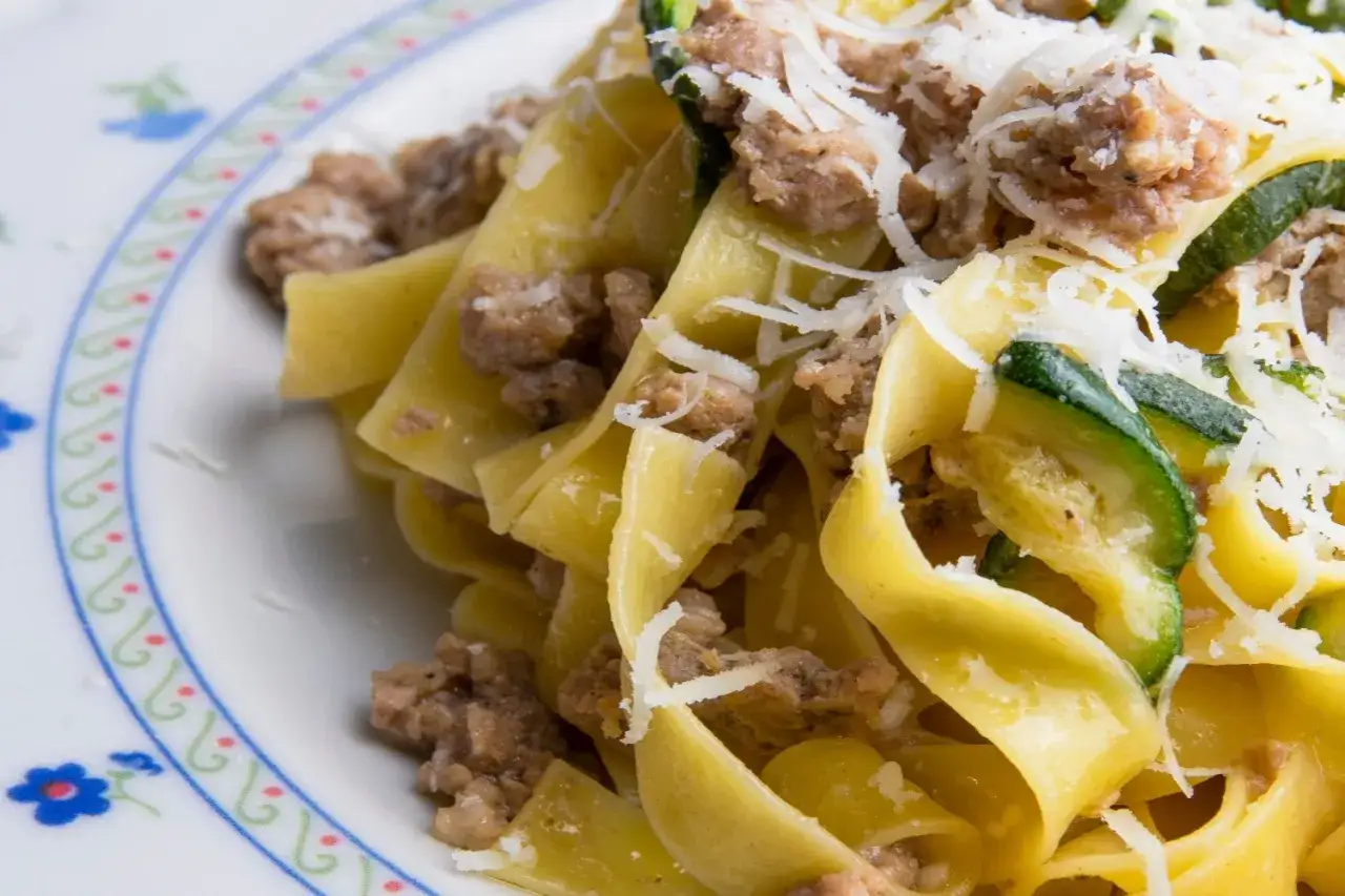 Piatto di pasta fresca con zucchine e salsiccia sbriciolata, condita con parmigiano grattugiato.