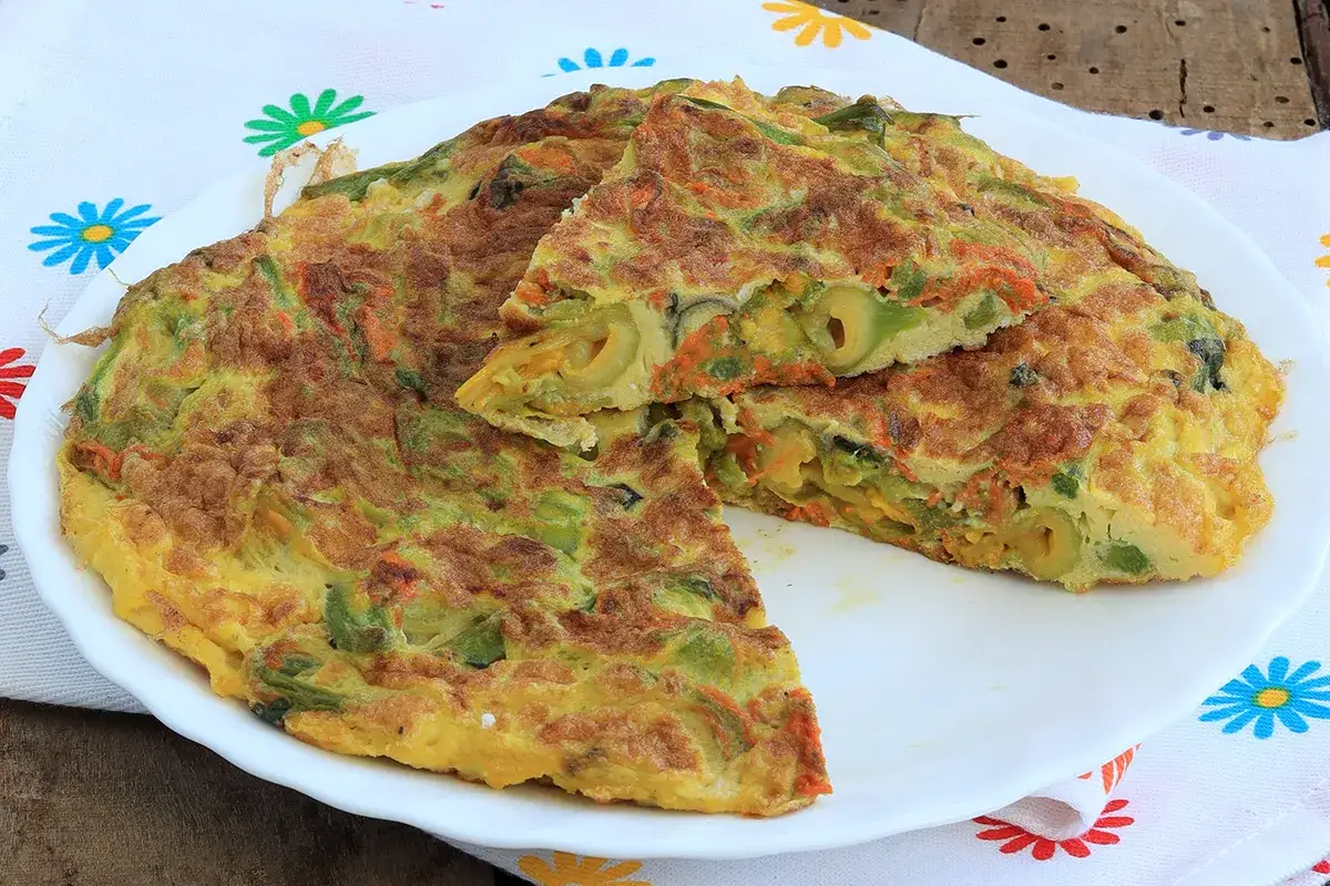 Frittata con fiori di zucca, carote e olive, tagliata a spicchi su un piatto bianco, su un tovagliolo colorato.
