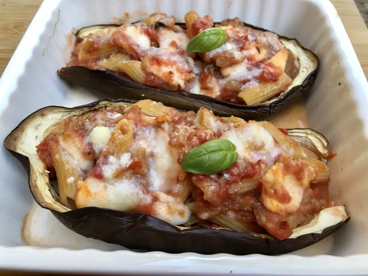Melanzane a barchetta ripiene di pasta al sugo e formaggio filante, guarnite con basilico fresco.