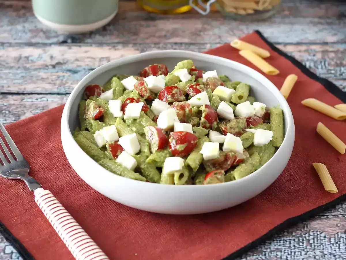 Un'appetitosa insalata di pasta con pesto, pomodorini e cubetti di mozzarella fresca, pronta per essere gustata.