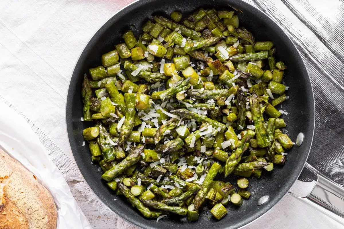 Asparagi in padella, tagliati a pezzi e conditi con formaggio grattugiato, pronti per essere gustati.