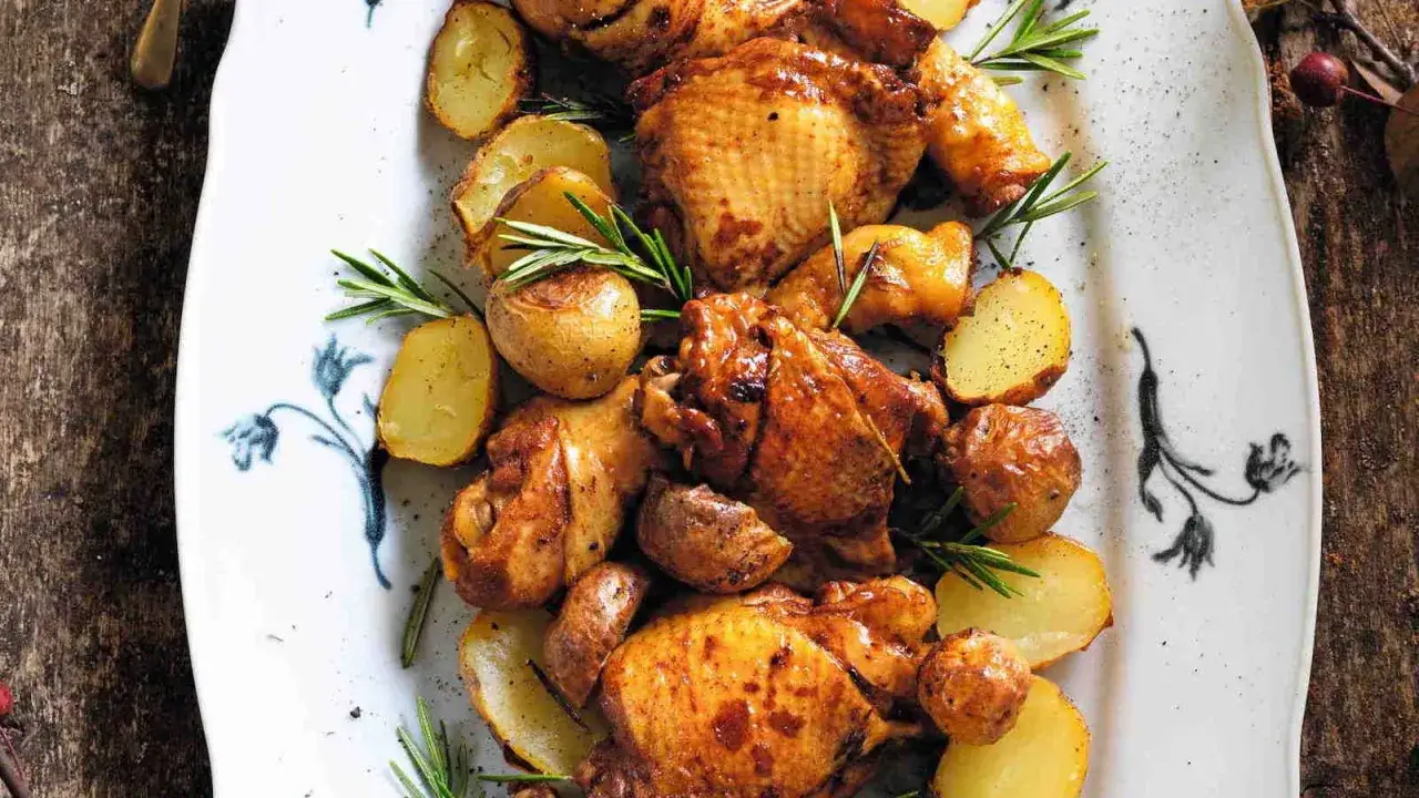 Succulento pollo alla birra con patate arrosto e rosmarino su un piatto bianco decorato.