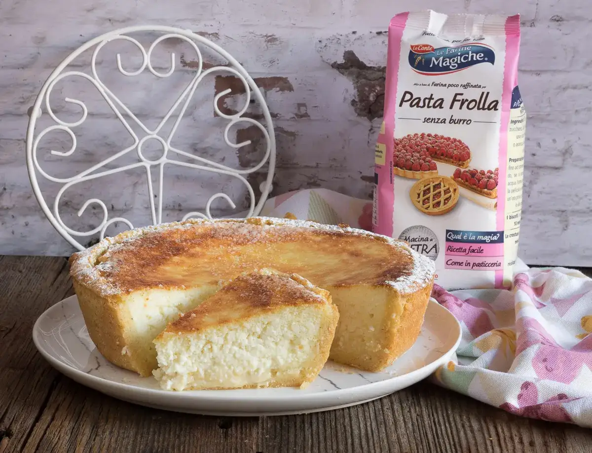 Deliziosa cassata al forno, con una fetta tagliata per mostrare il ripieno cremoso. Accanto, una confezione di farina per pasta frolla.