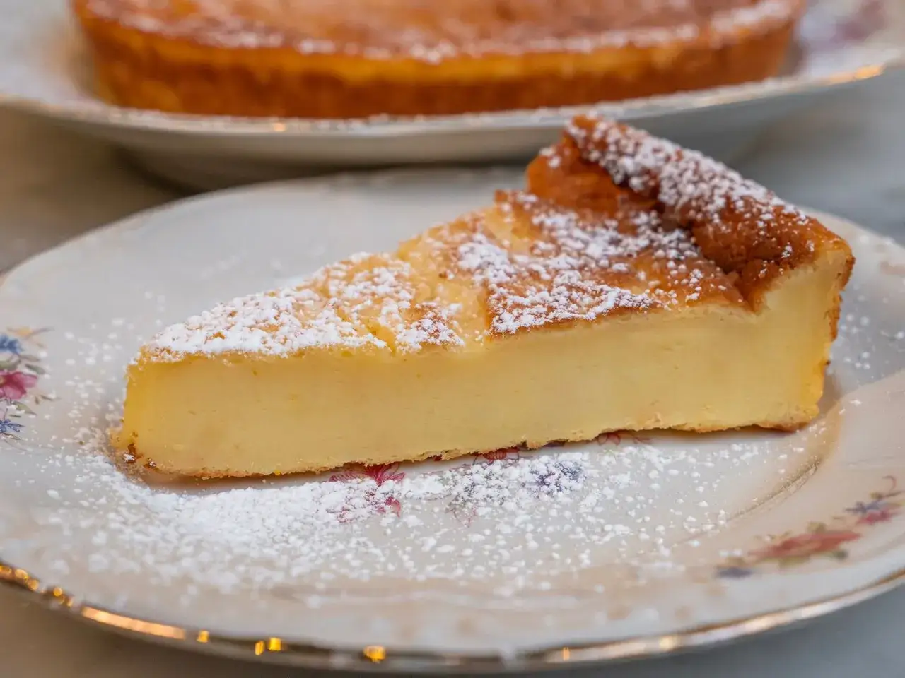 Una fetta di migliaccio napoletano ricetta della nonna, spolverata di zucchero a velo, su un piatto fiorito.