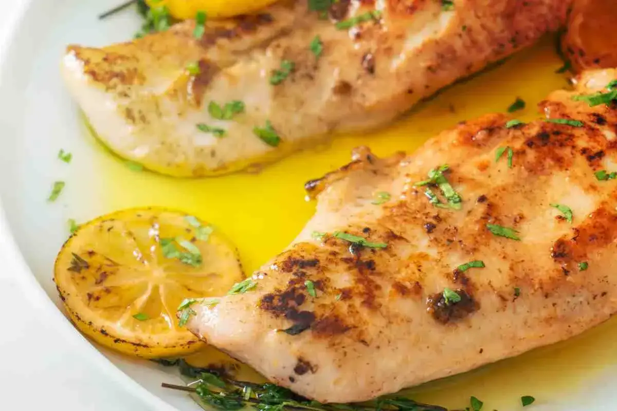 Delizioso pollo al limone dorato, guarnito con erbe fresche e fette di limone succose, servito in un piatto bianco.