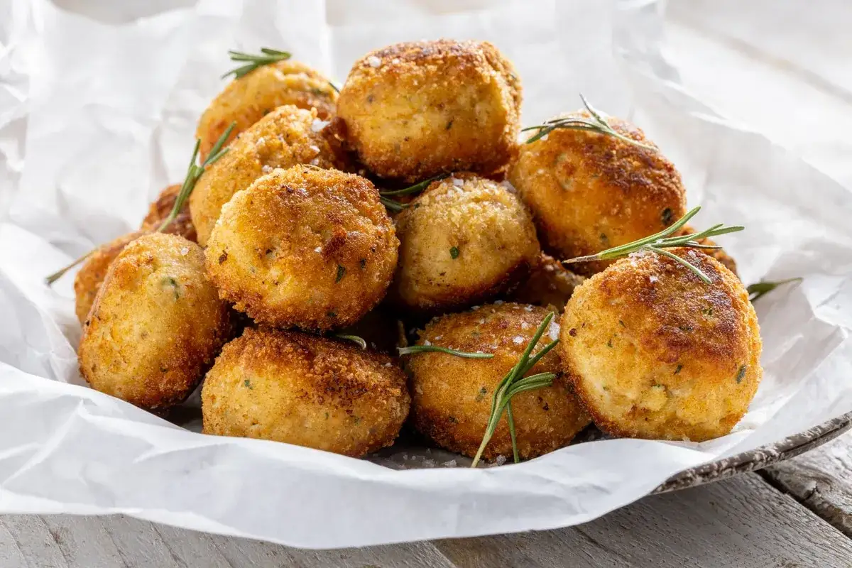 Pile di polpette in bianco dorate e croccanti, guarnite con rosmarino fresco e sale grosso.