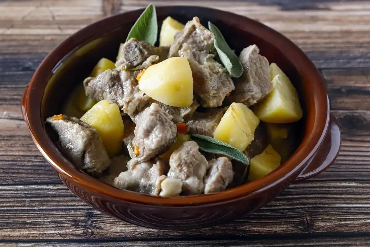 Un invitante spezzatino di manzo morbidissimo con patate e salvia, servito in una ciotola di terracotta su un tavolo di legno.