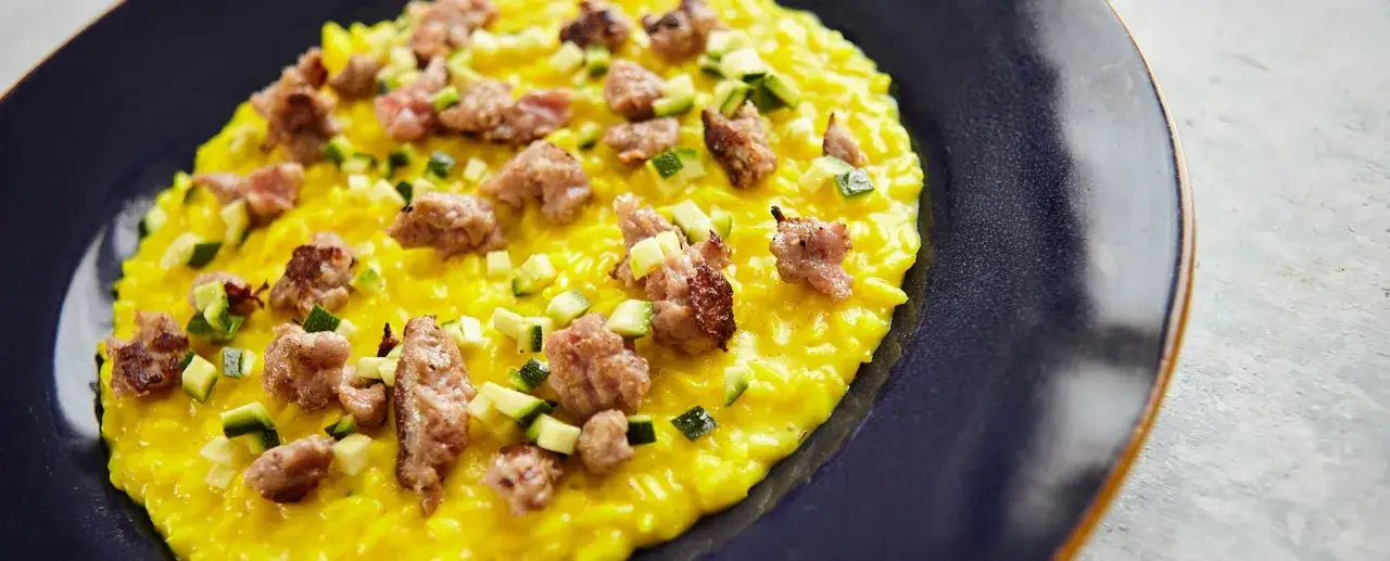Risotto giallo cremoso con pezzetti di salsiccia e zucchine croccanti, un piatto invitante.