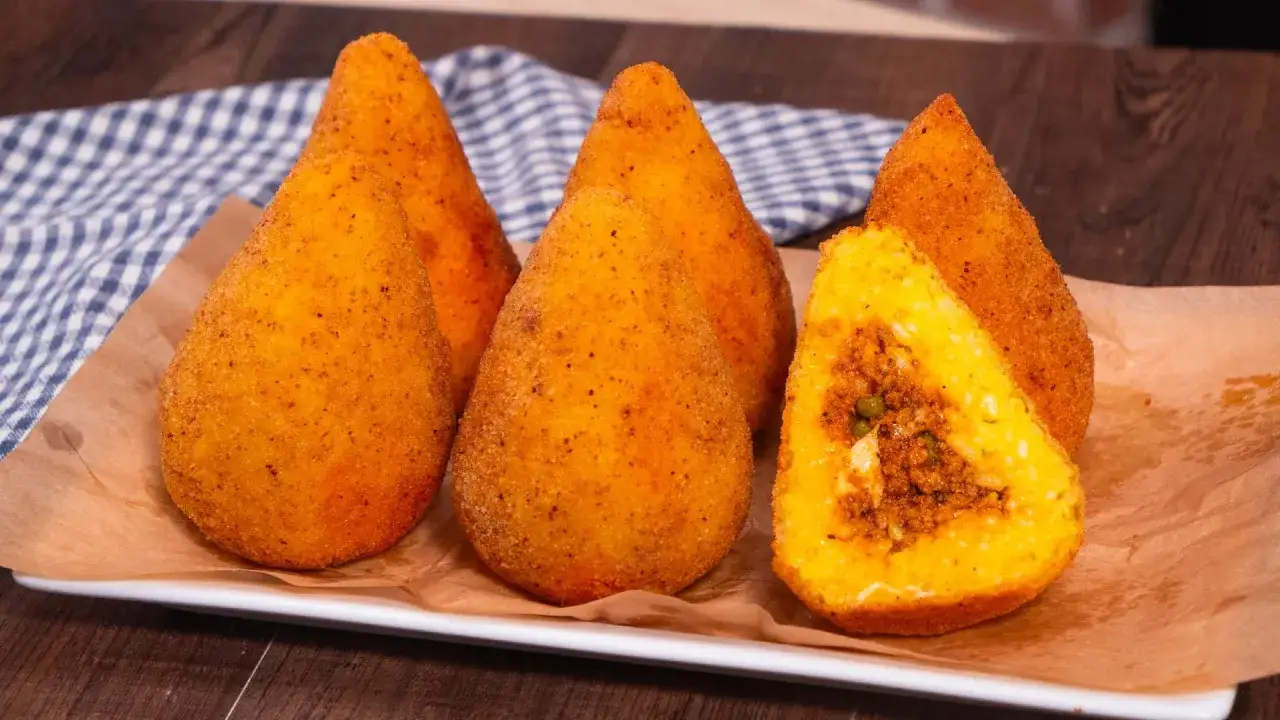 Cinque arancini di riso dorati e croccanti, uno tagliato a metà rivela un ripieno saporito.