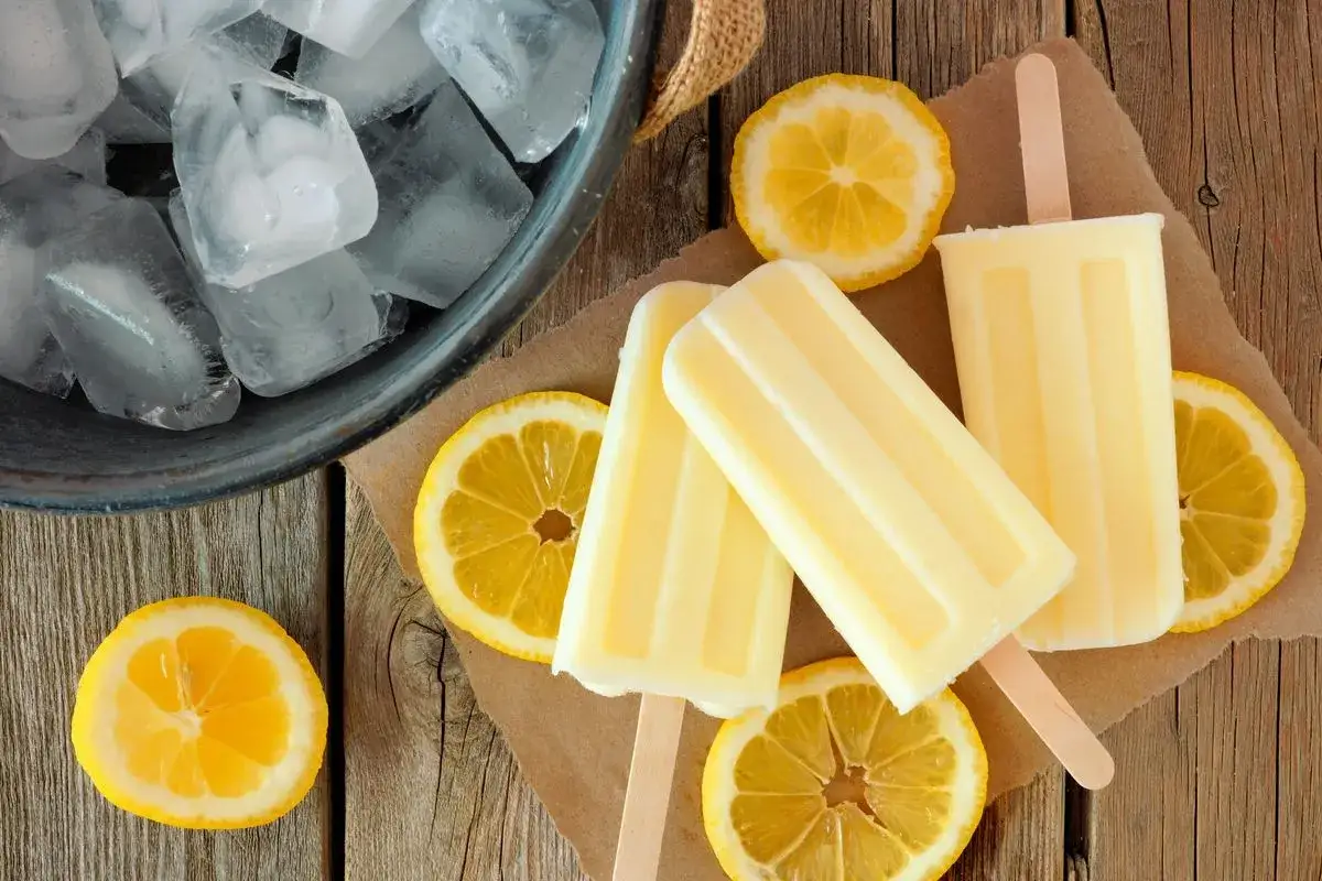 Ghiaccioli al limone freschi e succosi, pronti per rinfrescare una giornata calda. Circondati da fette di limone e cubetti di ghiaccio.