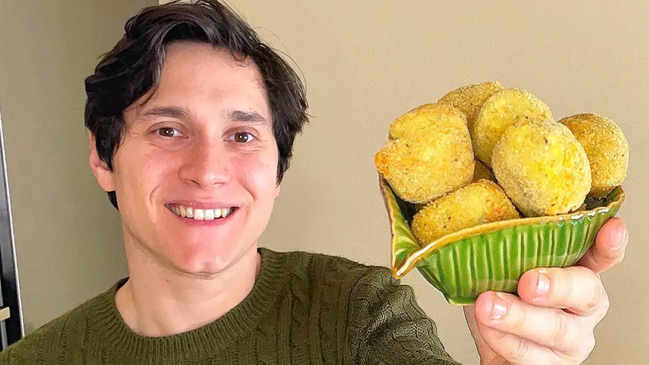 Un uomo sorride mostrando una ciotola verde piena di polpette di carciofi dorate e croccanti.