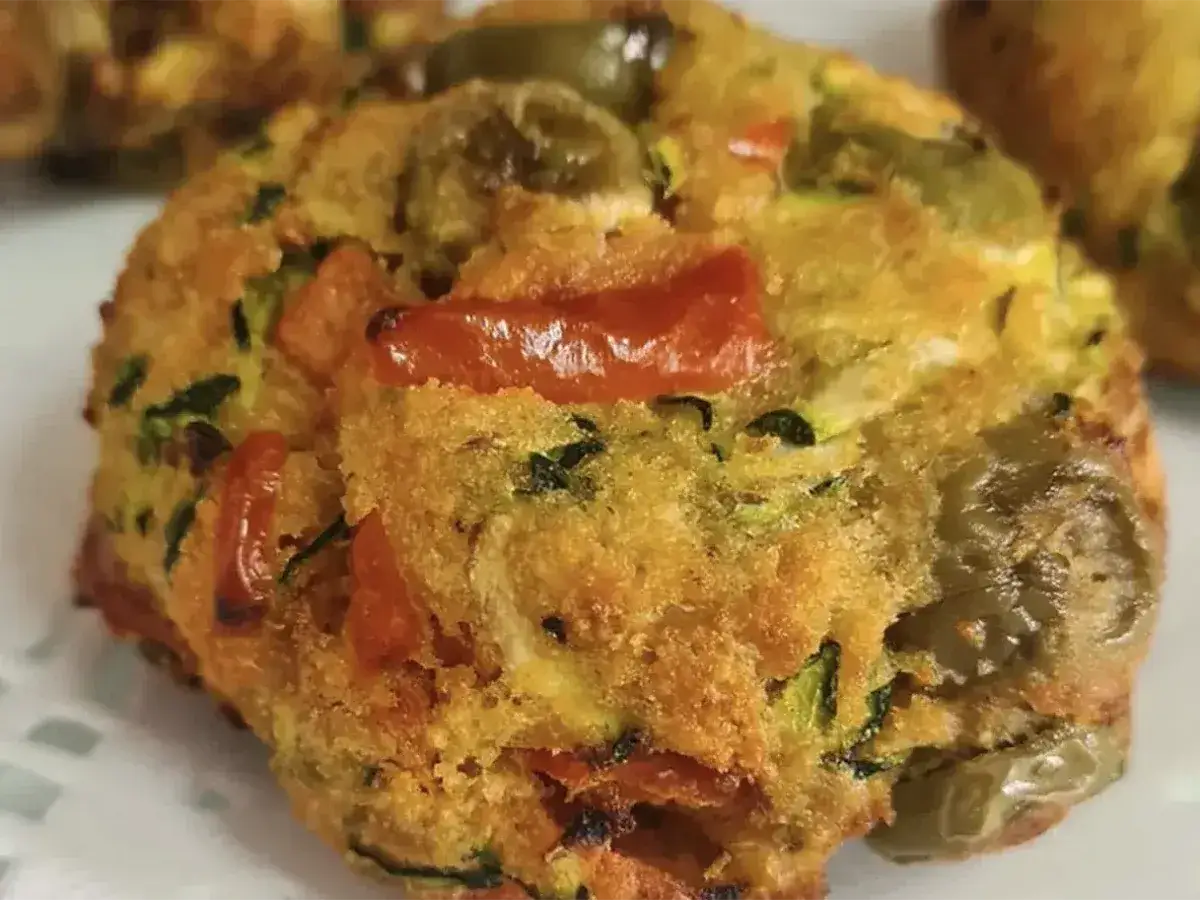 Polpette di zucchine dorate e croccanti, con pezzetti di pomodoro e olive verdi, pronte per essere gustate.