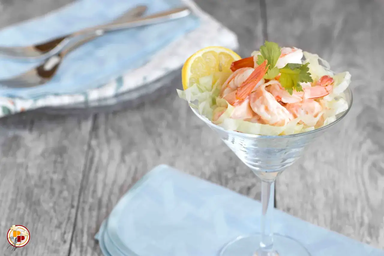 Un delizioso cocktail di gamberi servito in una coppa di cristallo, guarnito con limone e prezzemolo.