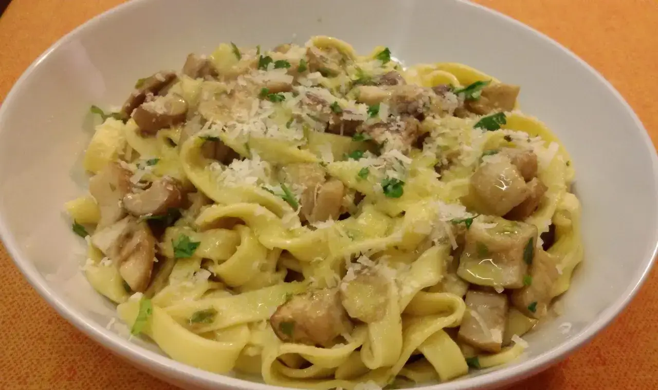 Un piatto invitante di tagliatelle ai funghi, condite con parmigiano grattugiato e prezzemolo fresco.