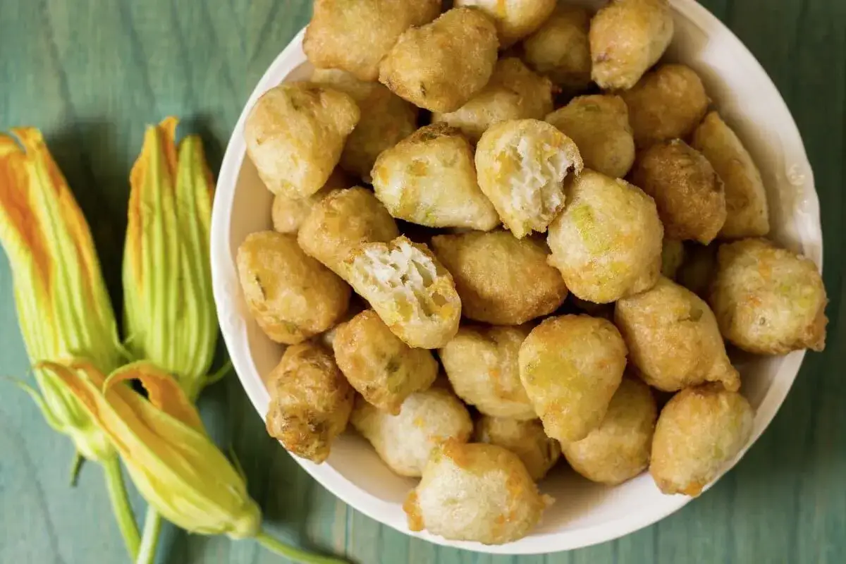 Frittelle dorate e croccanti, un delizioso antipasto di mozzarella in carrozza, accanto a fiori di zucca freschi.