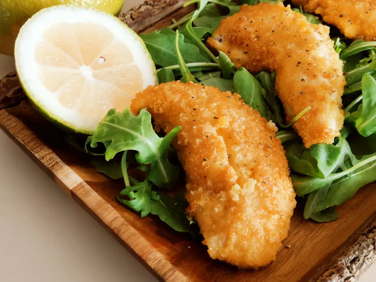 Croccante petto di pollo impanato su un letto di rucola, accompagnato da una fetta di limone.