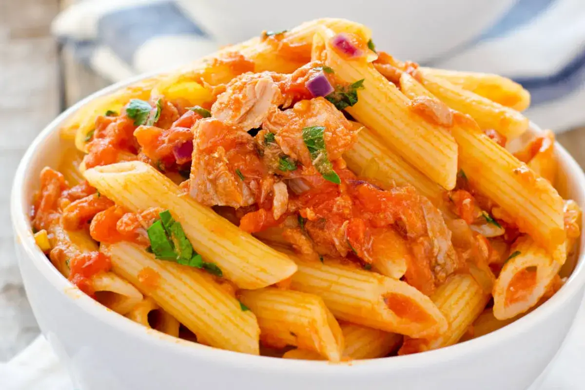 Penne al tonno in una ciotola bianca, condite con sugo di pomodoro, tonno e prezzemolo fresco.