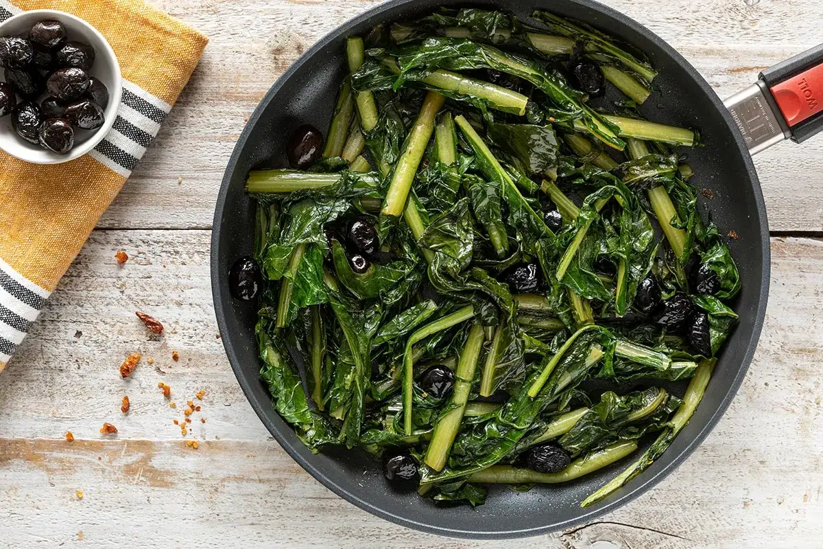 Cicoria in padella con olive nere, un contorno saporito e salutare, pronto per essere gustato.