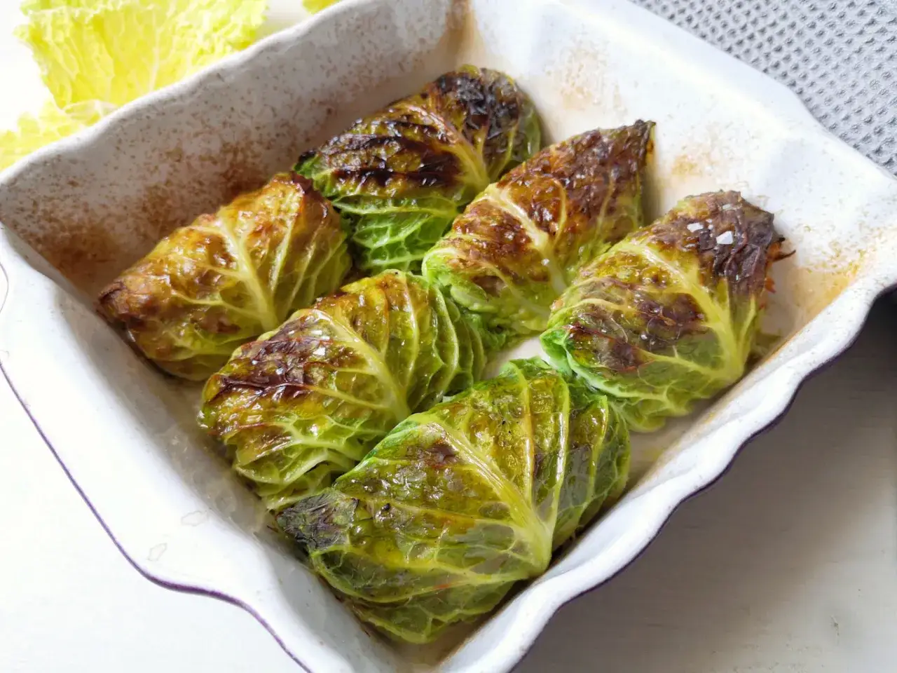 Involtini di verza con carne, cotti al forno e leggermente abbrustoliti, serviti in una teglia bianca.