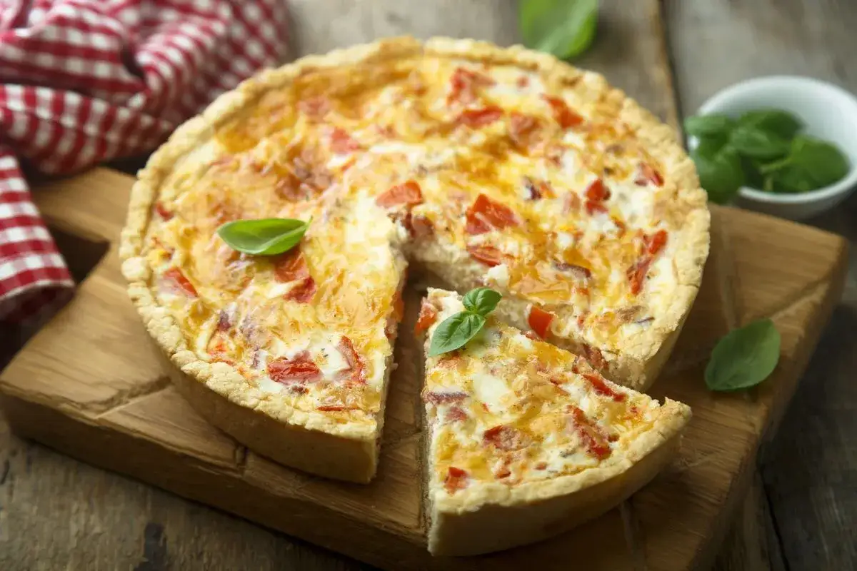 Una deliziosa torta salata patate e speck, con una fetta tagliata e guarnita con basilico fresco.
