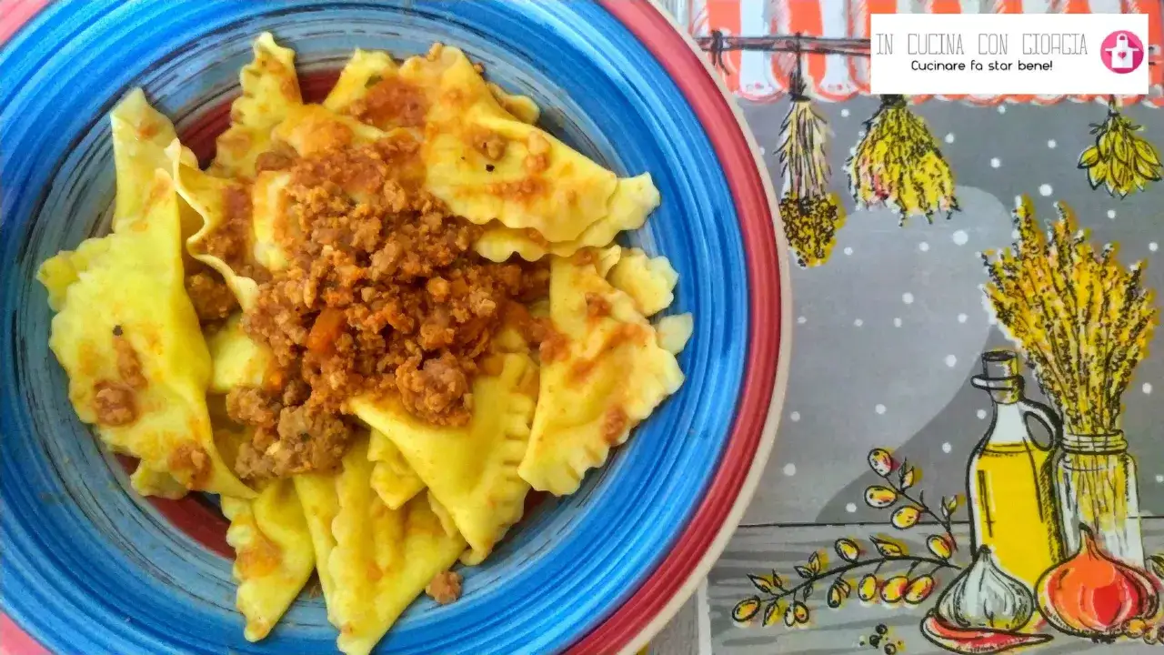 Tortelli di patate fatti in casa, conditi con un ricco ragù, serviti in un piatto colorato.