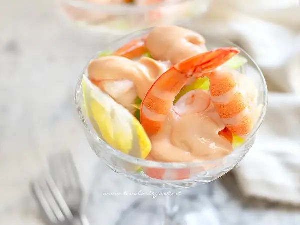 Un delizioso cocktail di gamberi servito in una coppa di vetro, con gamberi succulenti, salsa rosa e una fetta di limone.
