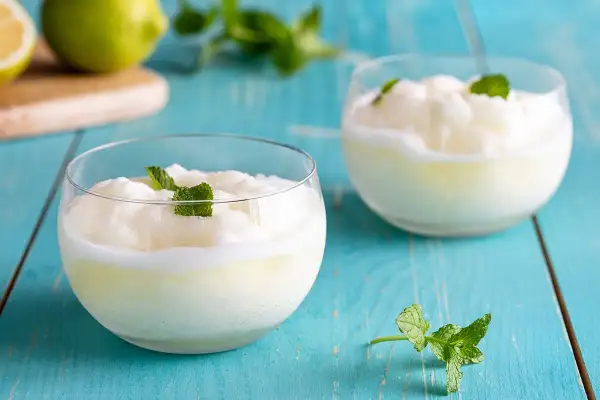 Due bicchieri di sorbetto al limone cremoso, guarniti con menta fresca, su un tavolo di legno blu.