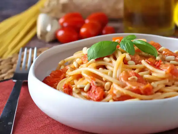 Un piatto invitante di spaghetti con pomodorini freschi, pinoli tostati e basilico, pronto per essere gustato.