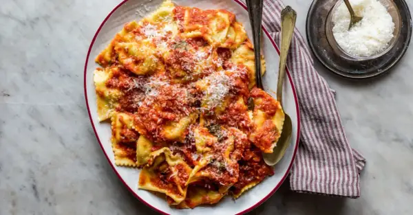 Piatto di tortelli di patate fatti in casa, conditi con sugo rosso e parmigiano grattugiato, pronti per essere gustati.