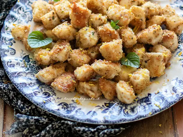 Bocconcini di pollo al forno dorati e croccanti, guarniti con scorza di limone e foglie di menta fresca su un piatto decorato.