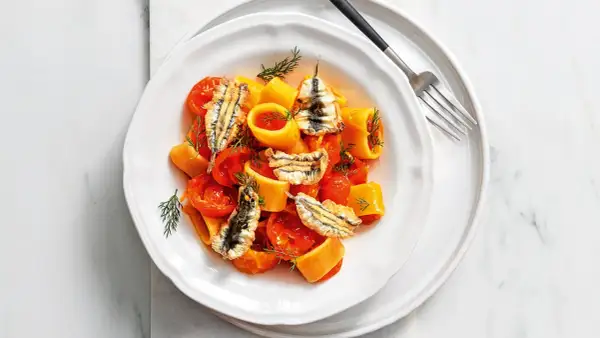 Piatto di pasta con pomodorini e croccanti alici fresche, guarnito con aneto.