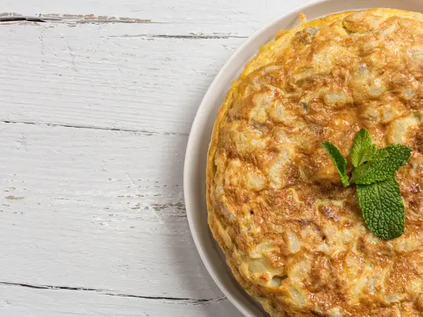 Frittata di cipolle dorata e soffice, guarnita con menta fresca, su un tavolo di legno bianco.