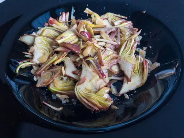 Un piatto nero lucido pieno di un'appetitosa insalata di carciofi crudi, tagliati finemente e conditi.