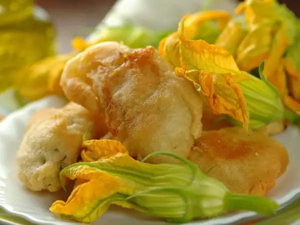 Fiori di zucca in pastella dorati e croccanti, guarniti con i loro stessi fiori freschi.