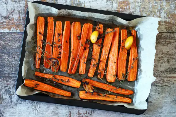 Carote al forno dorate e caramellate, condite con timo fresco, pepe nero e spicchi d'aglio arrostiti, pronte per essere gustate.