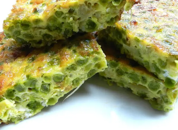 Fette di frittata di piselli, dorata e soffice, con piselli verdi ben visibili nell'uovo.