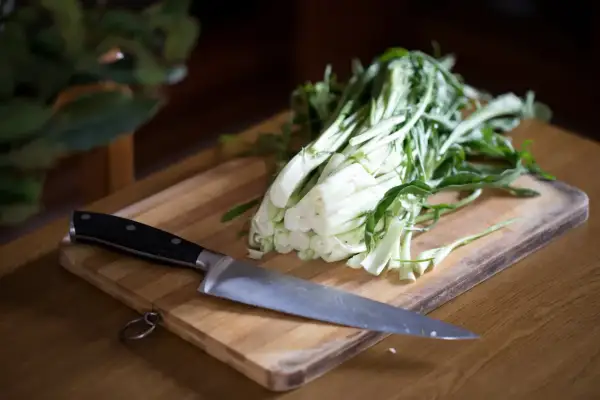 Un coltello affilato pronto a preparare le puntarelle alla romana su un tagliere di legno.