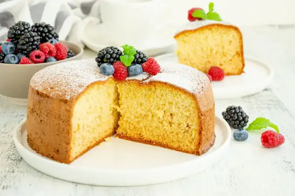 Una soffice torta senza zucchero, spolverata di zucchero a velo e decorata con frutti di bosco freschi, perfetta per una colazione leggera.
