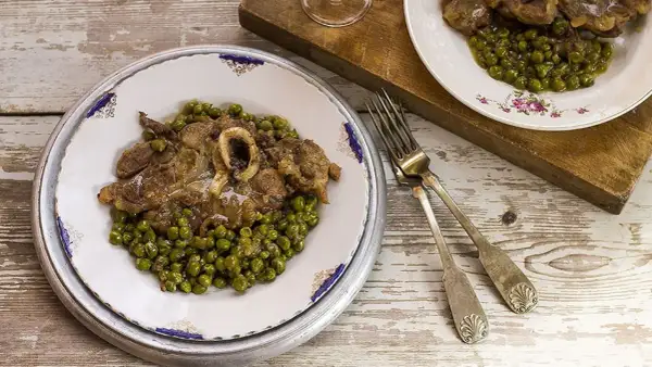 Un piatto di ossobuco con piselli, servito su un tavolo di legno rustico. Le forchette d'argento sono pronte per gustare questa delizia.