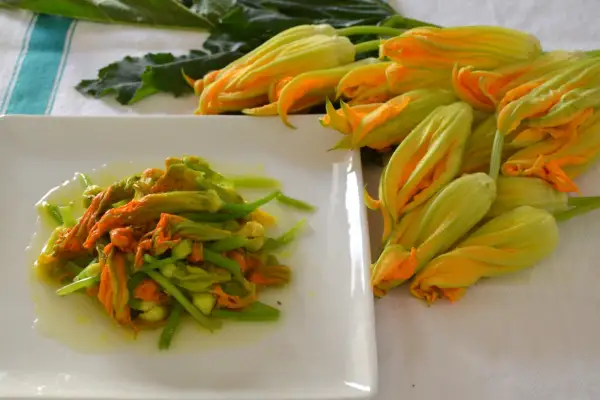Fiori di zucca in padella, un piatto primaverile pronto da gustare. Accanto, fiori freschi in attesa di essere cucinati.